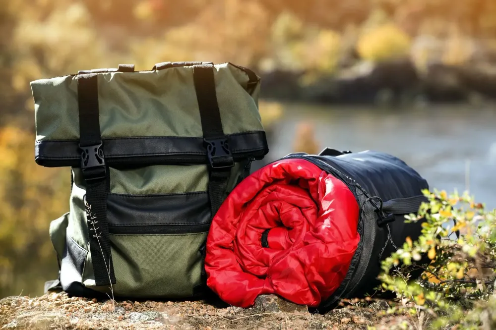 A sleeping bag and backpack on the ground in the woods